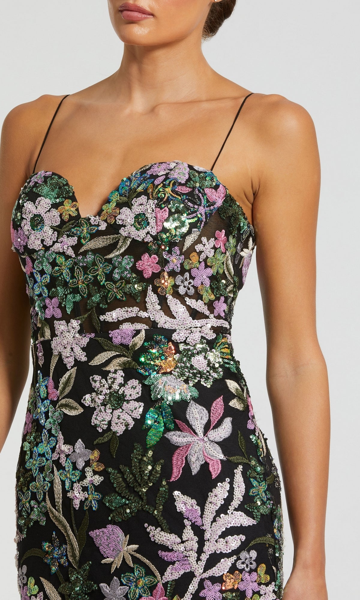 A woman wears the Mac Duggal 49827 Sequin-Print Black Formal Dress with thin straps and vibrant embroidery. The long formal gown shimmers as it catches the light, while her face is partially out of frame.